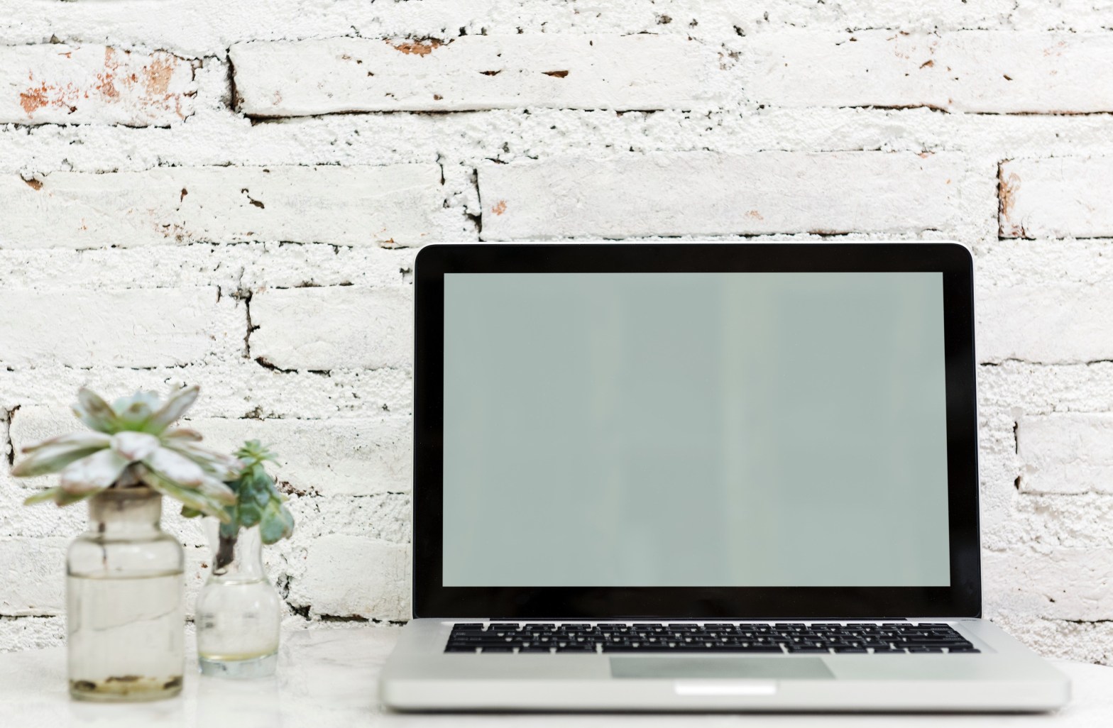MacBook Pro against white wall on a white desk with a few succulents in clear vases