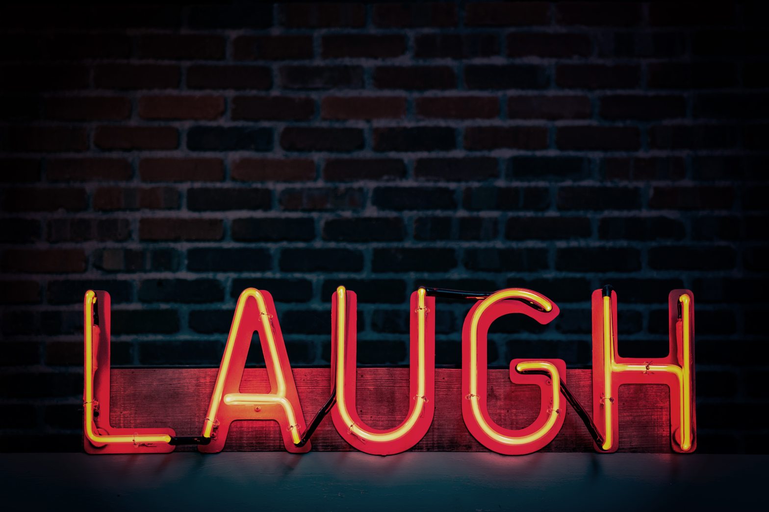 A read neon sign that reads "Laugh" stands in front of a brick wall.